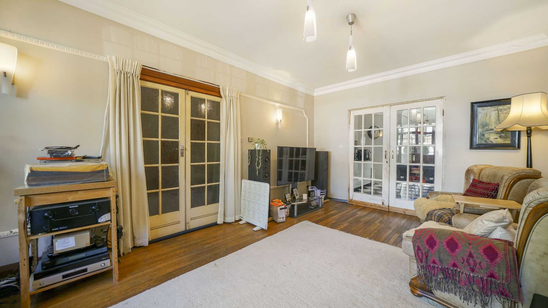 Bright living room with wooden flooring, French doors, armchair seating and television with speakers