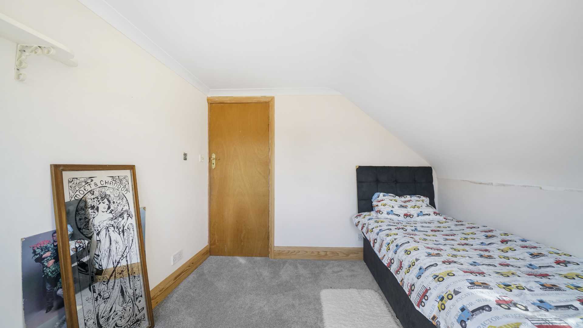Small bedroom with single bed, sloped ceiling, carpet flooring and wooden door